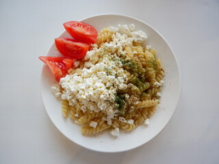 Pasta with cottage cheese, tomatoes and herbs on a white plate. White background