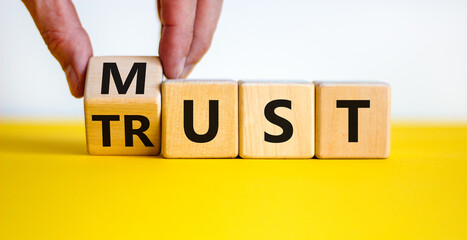 Must trust symbol. Businessman turns wooden cubes with words 'must trust'. Beautiful yellow table, white background. Business and must trust concept, copy space.