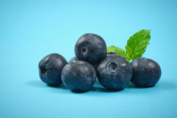 Blueberries isolated on a bluish background and with some green leaves in the background