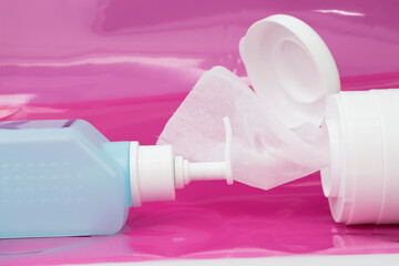 Infection control. Alcohol-based hand sanitizer in light blue bottle and disinfection wipes impregnated with alcoholic solution for surface disinfection on pink background