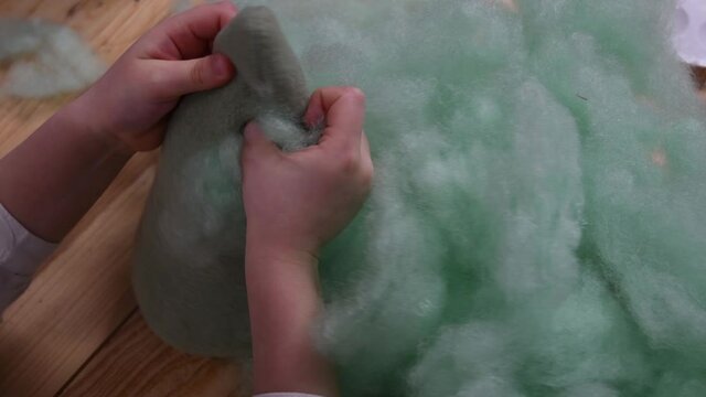 Toddler hands stuffing cotton inside felt toy. Green cotton sintepon hollow PP cotton filling material for making handicraft stuffed toys. Kids sensory crafting activity