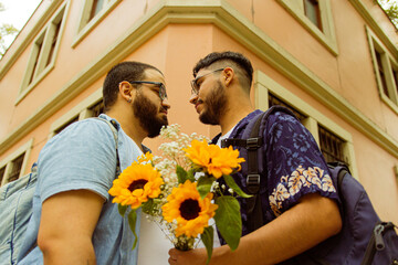 Pareja de novios gay mirándose cara a cara con un ramo de flores amarillas 
