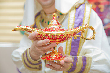 A man in Aladdin's clothes . A person holds in his hand realistic golden lamp of Aladdin . olds in his hands the magic lamp of Aladdin. holding an old magic lamp in his hand.