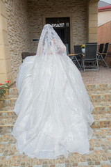 The bride takes a photo of the wedding dress from behind at home . the bride in a luxurious white dress stands near the window . The back side of a white wedding dress .