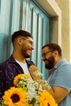 Pareja de novios gay riendo entre ellos en la calle con flores amarillas en la mano 
