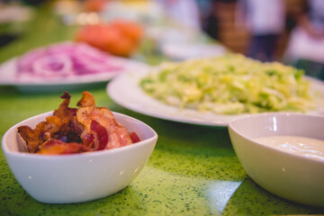 White bowls with fried bacon, lettuce, onion, mayo, tomato and other ingredients for burgers