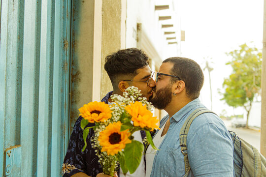 Retrato de pareja de novios gay besándose en la calle con flores amarillas en la mano 
