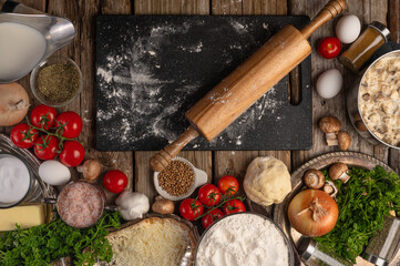 Pizza making process. Flour, turkey meat, chicken meat, tomatoes, onions, eggs, garlic, spices, cutting board, rolling pin. Scenic close-up. View from above. Daylight