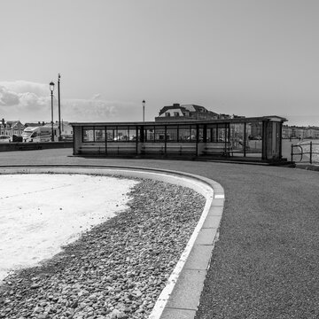 A black and white photograph showing the public paddling pool in Llandudno is emptied and lies abandonded full of pebbles from the beach