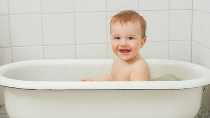 Little happy toddler bathes in a bathtub