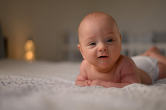 Adorable smiling baby wearing diapers while lying in bed on a tummy