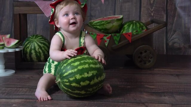 Girl in green romper on wooden background looking at a watermelon.