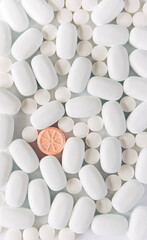 White pills on a white background. One bright orange round pill accent. Oblong and round pills close-up. Healthcare and medicine.