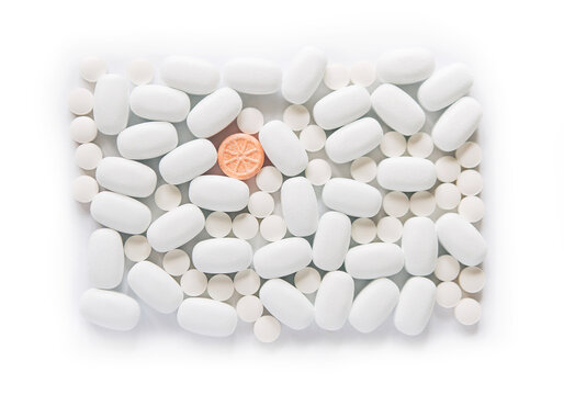 White pills on a white background. One bright orange round pill accent. Oblong and round pills close-up. Healthcare and medicine. © Olena Svechkova