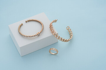 Golden bracelets and ring on white box on blue background with copy space