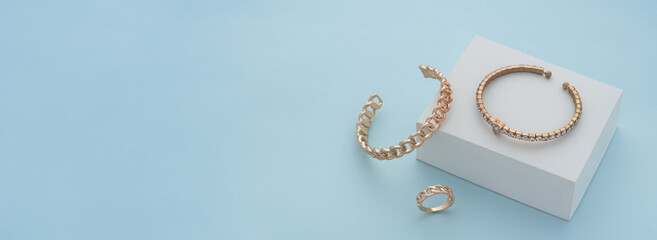 Panoramic shot of golden bracelets and ring on white box on blue background - obrazy, fototapety, plakaty