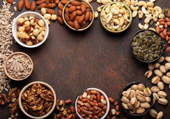 Obraz na płótnie Canvas Selection of assorted raw nuts and various seeds in bowls on brown stone background from above, healthy source of energy, fat and vegetarian protein, space for text