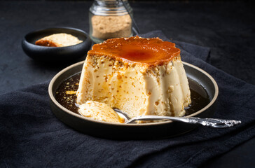 Modern style traditional creme caramel pudding served as close-up in a Nordic design plate on black background