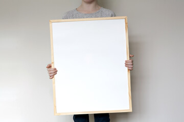 Child holding a large, thin wooden frame mockup template. Horizontal orientation.