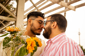 Retrato detalle de pareja de jóvenes gay mirándose a punto de besarse sosteniendo flores...