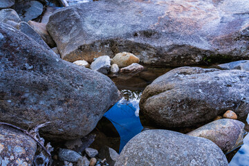 Fototapeta na wymiar Reflection of the sky on the surface of the crystal clear Pemigewasset River among huge smooth stones in spring. Franconia Falls by the Lincoln Forest Trail in the White Mountains National Forest, NH