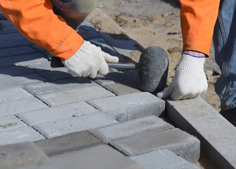 A worker knocks on paving slabs, levels a concrete block with a construction hammer, close-up.