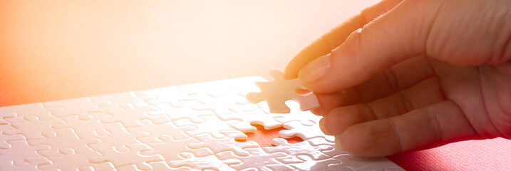 Hand inserting last missing puzzle on red background, business concept - obrazy, fototapety, plakaty