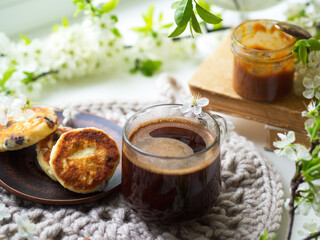Spring time, a cup of aromatic espresso coffee in a glass cup, cheesecakes and salted caramel. Blooming branches of white cherry