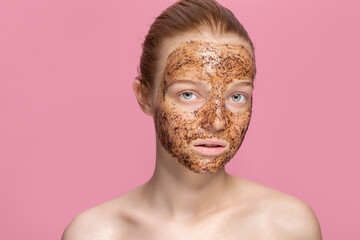 Facial skin scrub Coffee grounds mask on the face of a beautiful young woman Organic natural cosmetology Pink studio background Isolate