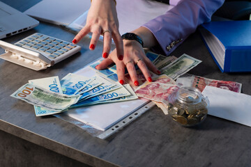 Female manicured hands with red nail polish reach for a heap of money. Dollars, british pounds sterling and new shekels banknotes on the table. Concept of success, greed and corruption, lust for money