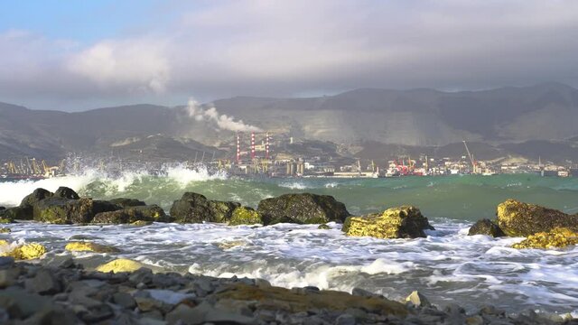 Stone coast. Gold stones. Sea water. Azure water. Waves roll onto the shore. Splashing water. Against the background of the mountain. There are industrial enterprises on the shore. Smoking chimneys. E