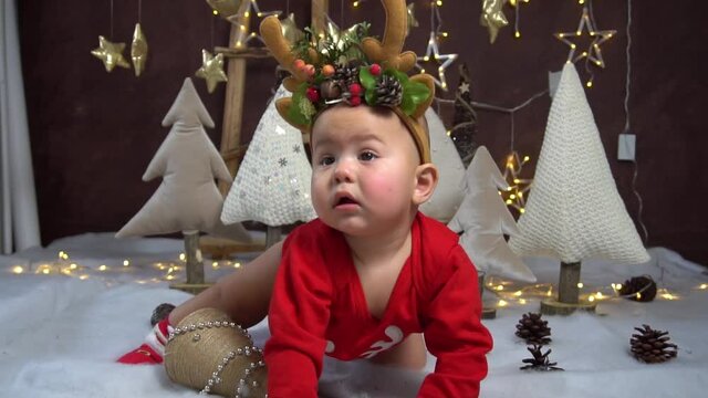 Cute baby in Christmas costume and Christmas decorations on floor at home.