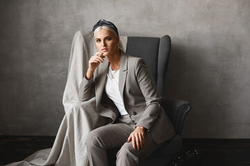 Close-up portrait of a young Caucasian woman with blond hair looking at camera while sitting in the armchair. Gorgeous young businesswoman in stylish suit posing in an empty interior