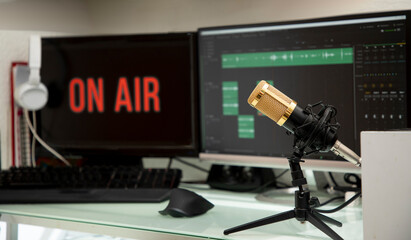 Mesa de trabajo de Blogger, con micrófono y computadora para transmisión de podcast en lineá, con anuncio al aire y monitores