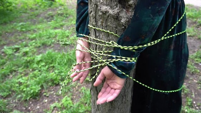 Slow Motion Restraint Of Women Concept. A Woman With Her Hands Tied To A Tree.