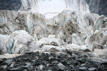 Fototapeta na wymiar The huge Ak-Kem glacier in Altai at the foot of Mount Belukha, close-up of white ice with cracks, gray stones in the foreground, in the background a rock with a glacier