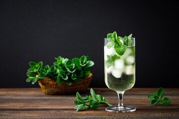 Iced mint tea, refreshing herbal drink in a glass with ice and fresh leaves on dark background