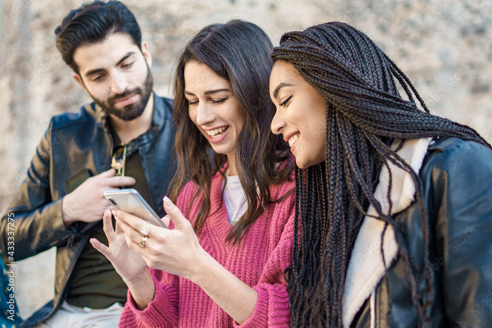 Wall mural Group of three interracial best friends using smartphone and social networks online