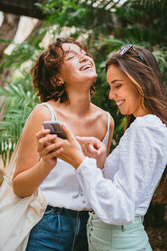 Two teenager girls are looking and pointing at a mobile phone. They are laughing at and talking about a photo that they received.