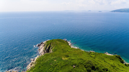 The reserved island of Furugelma on the ege of Primorsky Krai. View from above. Beautiful green island against the background of the blue sea.