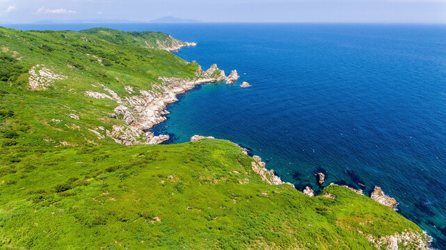 The reserved island of Furugelma on the ege of Primorsky Krai. View from above. Beautiful green island against the background of the blue sea.