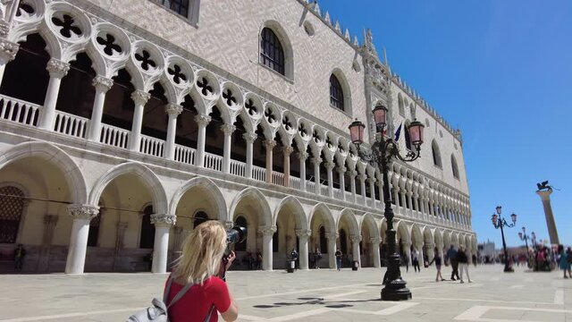 Italian girl in red taking pictures in Saint Mark square of Venice with winged lion column. Saint Mark Basilica of Venetian city. People with surgical mask for Coronavirus Covid-19 pandemic