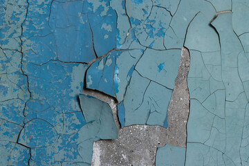 Blue peeling paint on the wall. Old concrete wall with cracked flaking paint. Weathered rough...