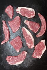 Various Raw Steaks. Sirloin Beef Steaks, Overhead View. Many Raw Striploin Steaks from Marbled Beef on Black Background. Group of Black Angus Beefsteaks. Raw Sirloin Cuts. Uncooked Prime Beef Steaks.