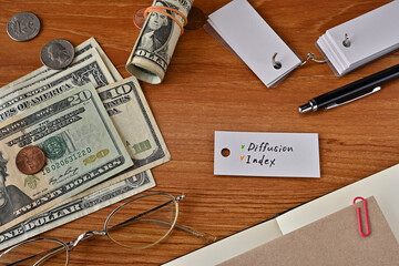 There is a word book with the word Diffusion Index which is a financial term written on it. It is on a desk with bills, glasses and notebook.