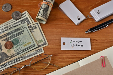 There is a word book with the word foreign exchange which is a financial term written on it. It is on a desk with bills, glasses and notebook.
