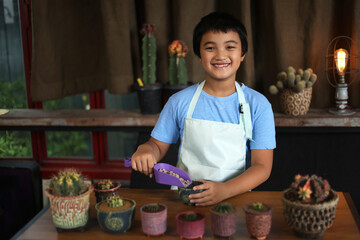 Asian boy make mini gardening cactus in the colorful pottery little cactus pot . Home gardening hobby concept. Selective focus.
