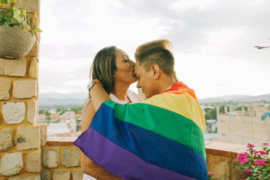Madre besa la frente de hijo gay quien porta la bandera LGTBQ