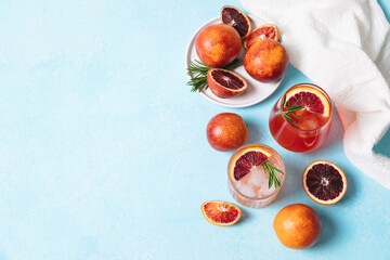 Blood orange cocktails with fresh fruits on blue table background. Summer cocktails, lemonade, refreshing drinks, low alcohol mocktail, party concept. Flat lay, top view, copy space.