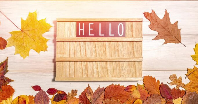 Stop motion animation of a wooden letter board with a set of text phrase Hello Autumn, red ripe apple and dry fallen leaves on a wooden background. Autumn season, harvest time, leaffall, fall concept.